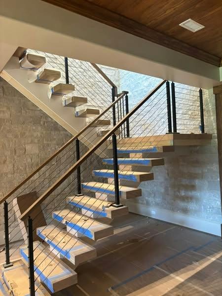 Interior stair with wood treads and dark railing; clear glass panel along the stair run